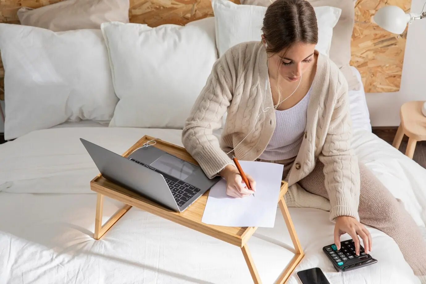 Medium shot of a woman working in bed.