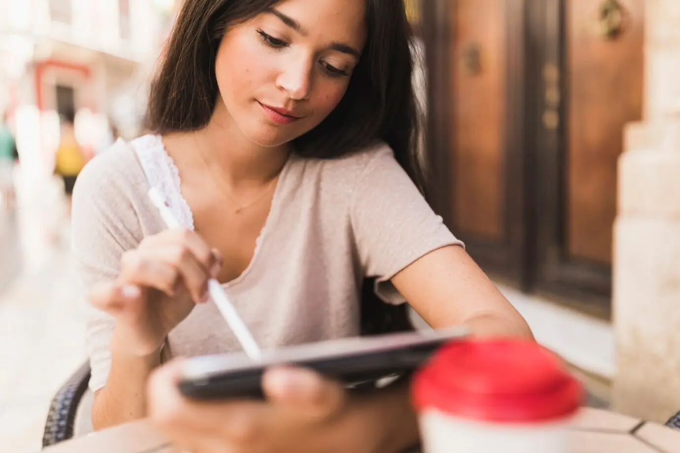 At an outdoor café, a teenage girl uses a stylus on a digital tablet.